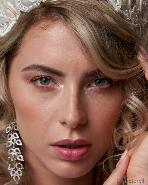 Close-up portrait of a woman with warm-toned makeup and ornate dangling earrings.