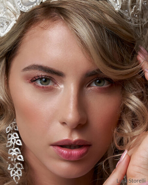 Portrait of a woman with styled wavy hair, dramatic eye makeup, and ornate dangling earrings.