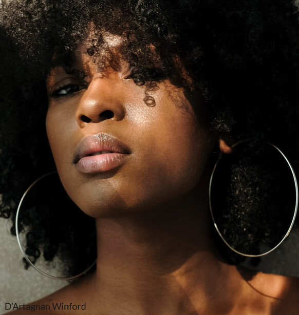 Portrait of a woman with textured hair against a dark background, wearing large hoop earrings.
