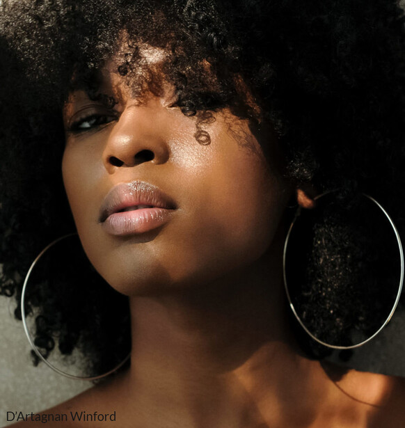 Portrait of a woman with textured hair and hoop earrings against a dark background.