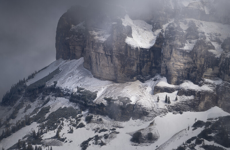 Snow-covered mountain with dramatic rocky peaks shrouded in mist and clouds.