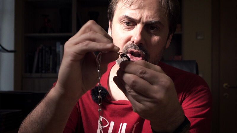 Man in red shirt examining prayer beads closely with concentrated expression.