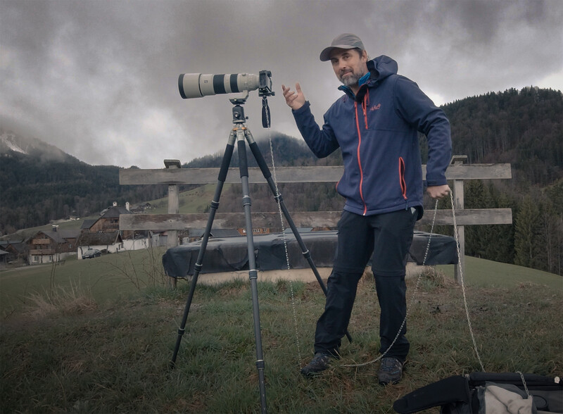 Photographer using a telephoto lens on a tripod in a mountainous valley landscape.