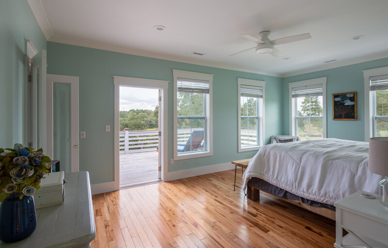 Bright bedroom with turquoise walls, hardwood flooring, and multiple glass doors opening to a deck overlooking water.