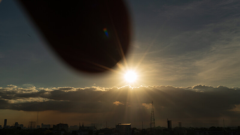 Bright sun breaking through dark storm clouds above an urban skyline at dusk.
