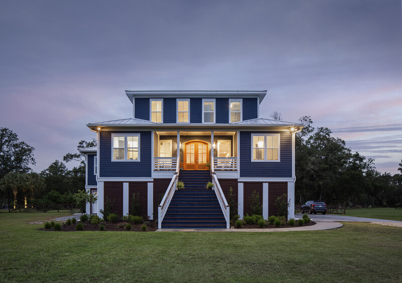 Modern elevated home with dark blue exterior and golden-hour lighting at dusk.