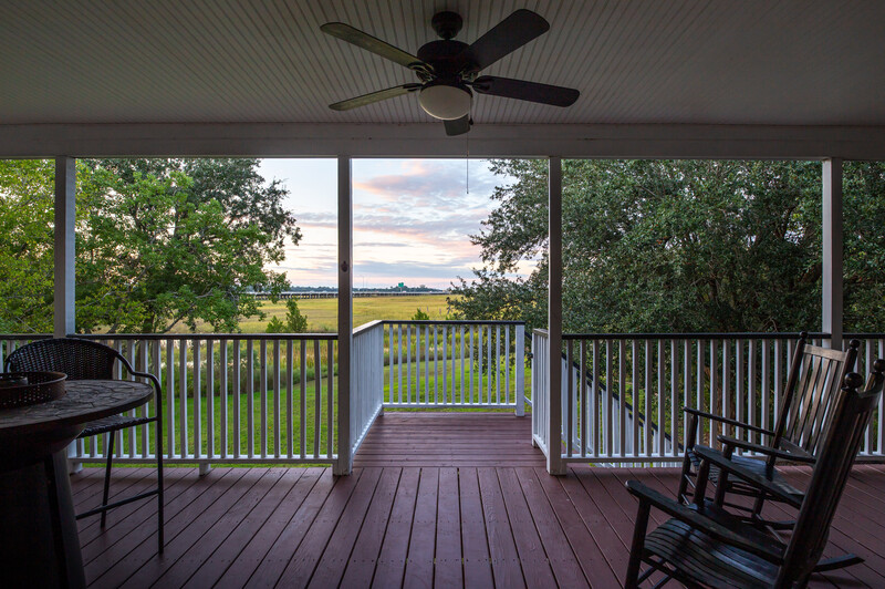 Covered porch with dark wood decking and white railings overlooking a pastoral landscape at golden hour.