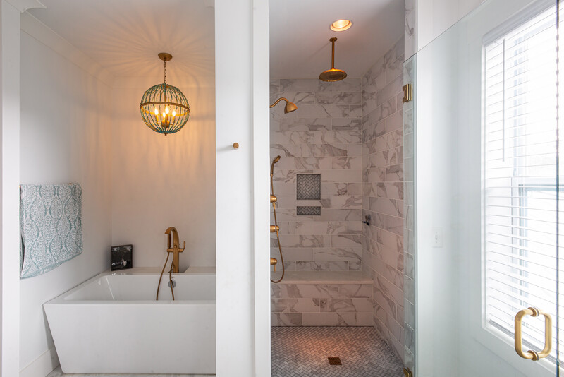 Modern bathroom split-view showing soaking tub with pendant light on left and walk-in shower with marble tile on right.