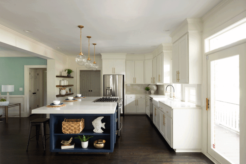 Modern kitchen with white cabinetry, blue island, and pendant lighting overlooking adjacent room.