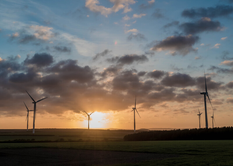 Wind turbines silhouetted against a dramatic sunset sky with golden and blue tones.