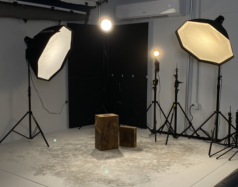 Professional photography studio setup with two octagonal softboxes, black backdrop, and wooden posing boxes on white floor.