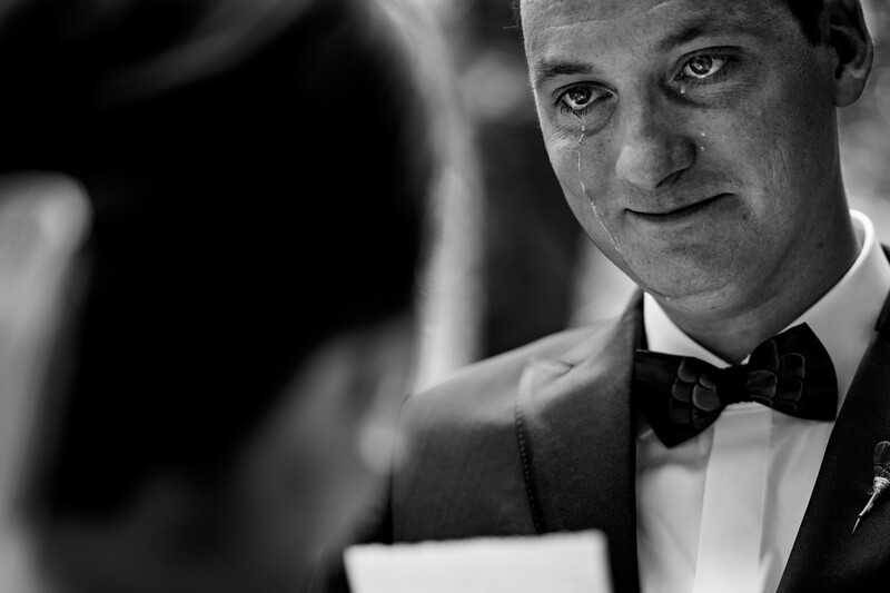 Man in formal tuxedo with bow tie looking directly at camera in black and white portrait.
