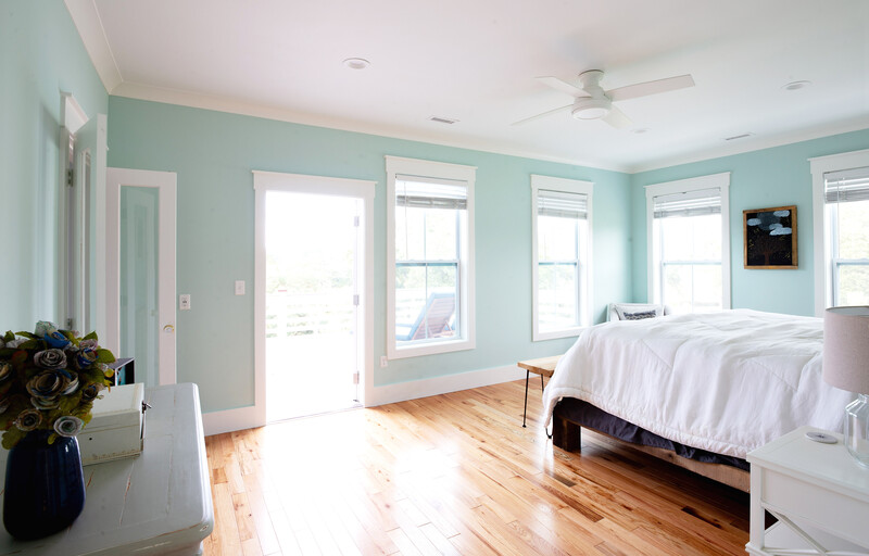 Bright bedroom with turquoise walls, hardwood floors, and multiple windows flooding the space with natural light.