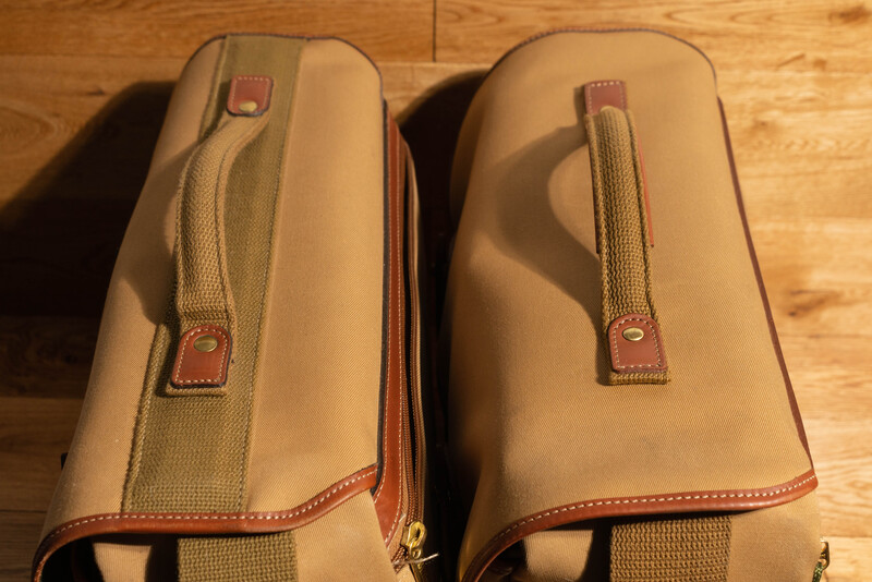 Two tan canvas and leather camera bags with handles and brass hardware displayed on wooden flooring.