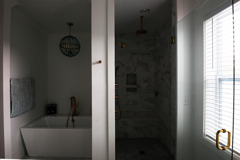 Modern bathroom with freestanding white tub, walk-in shower with dark tile, and natural light from window with shutters.