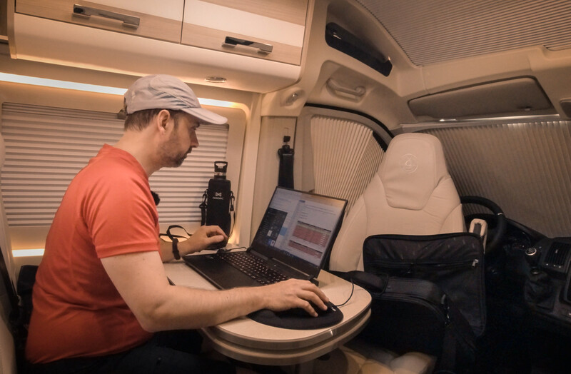 Man working on a laptop inside a compact RV or camper van interior.