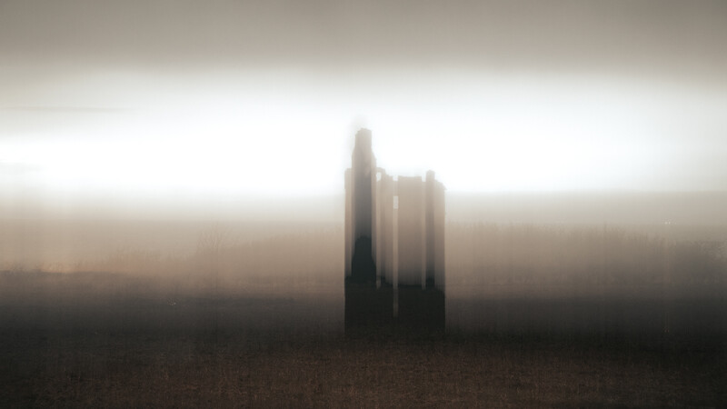 Architectural structure emerging from thick fog in a barren landscape.