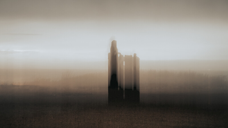 Silhouetted tall structures emerging from thick fog in a barren landscape.