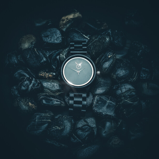 Black digital watch with circular dial centered on dark rocks and rubble.