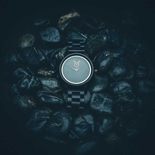 Dark-themed product photography of a digital watch surrounded by scattered mechanical parts and debris.