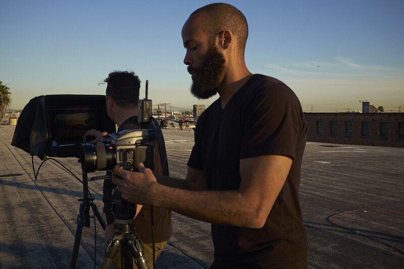Cinematographer operating a camera on a rooftop at golden hour with city skyline in background.