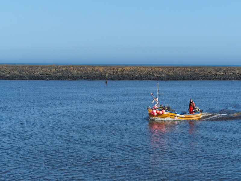 Yellow and red fishing boat on calm blue water with rocky breakwater and clear sky.