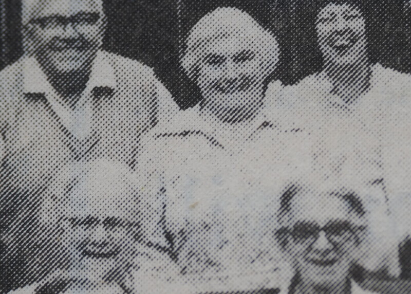 Grainy black and white photograph of five people posing together outdoors.