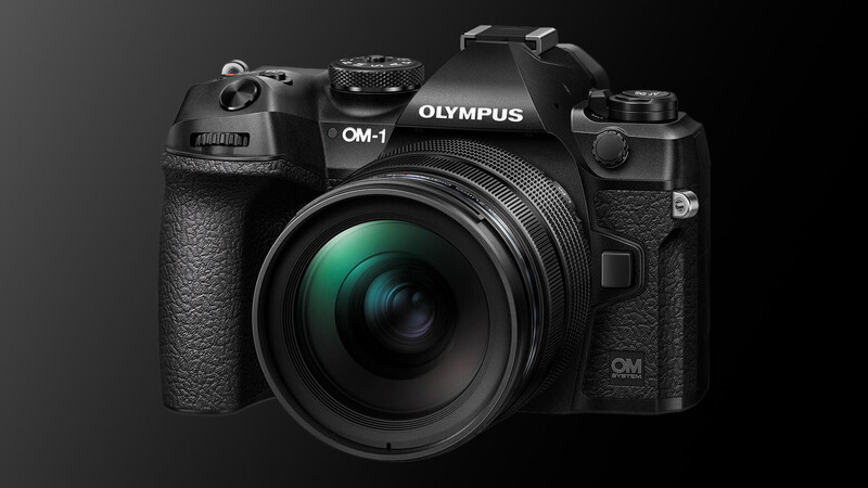 Olympus OM-1 mirrorless camera with attached lens against dark background.