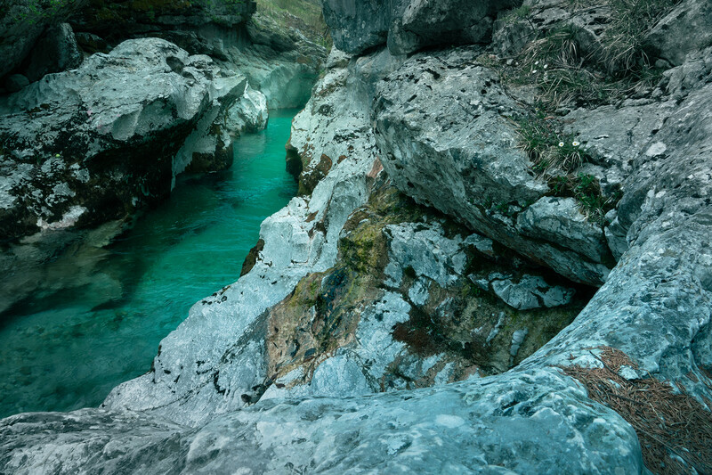 Turquoise river flowing between layered limestone rock formations with white mineral deposits.