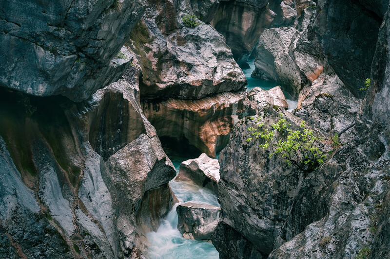 Turquoise river flowing through narrow rocky canyon with moss-covered stone walls.