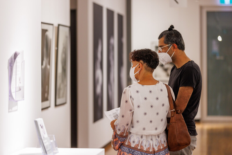 Adult and child wearing masks view framed artwork on a gallery wall.