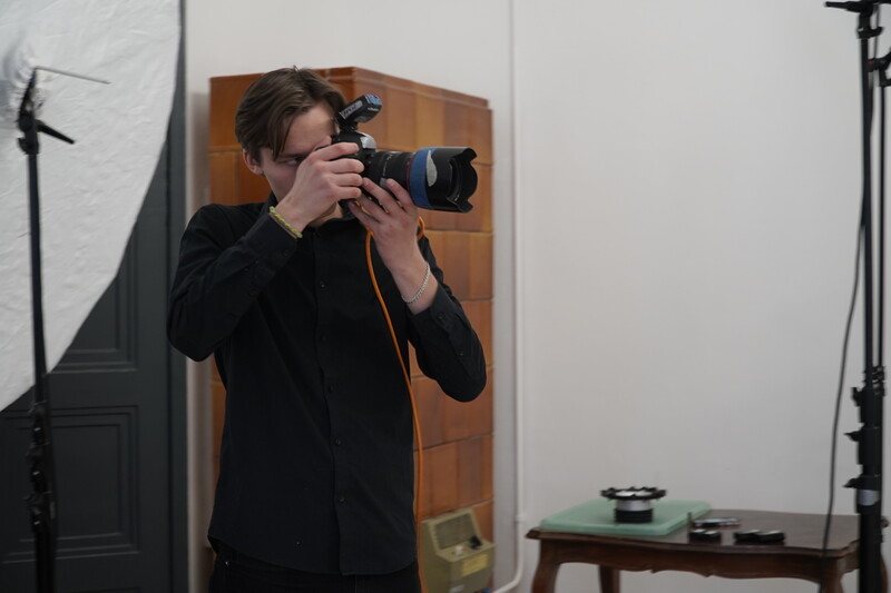 Photographer holding a DSLR camera with telephoto lens in a studio setting with professional lighting equipment.