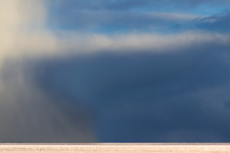 Dramatic storm clouds gathering above a flat, empty horizon under clearing sky.