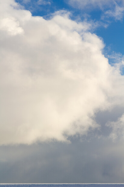 Towering cumulus cloud formation against blue sky with wispy clouds.