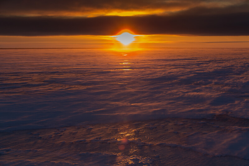 Bright sun on horizon above a sea of clouds at golden hour, shot from above the cloud layer.