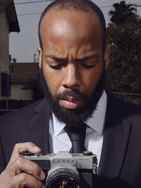 Man in formal business attire examining a vintage rangefinder camera outdoors.