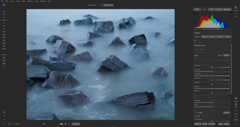 Rocky coastline with boulders partially submerged in misty seawater under blue twilight conditions.