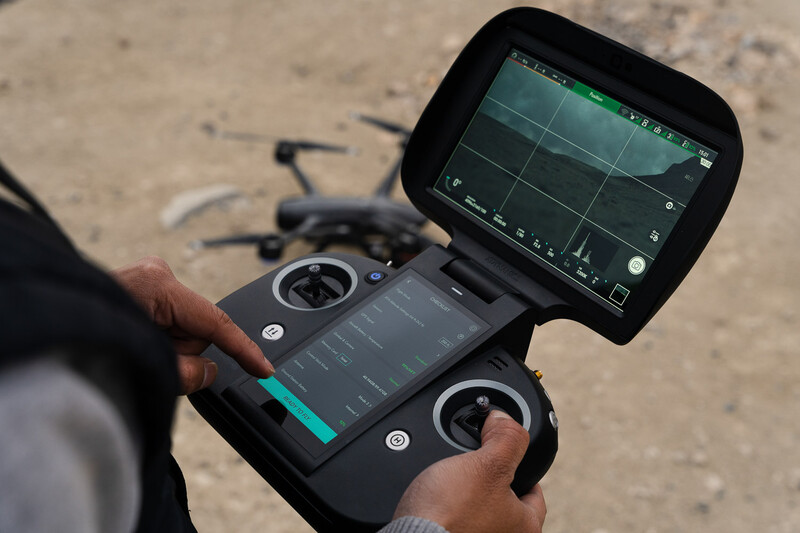 Drone remote controller with screen displaying camera feed and flight controls held by operator outdoors.