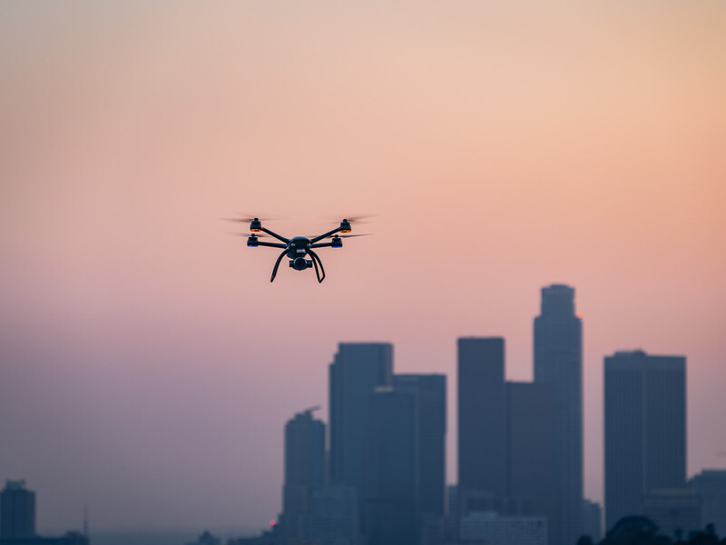 Drone flying against a pink and purple twilight sky above a silhouetted city skyline.