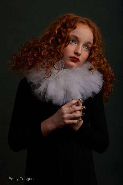 Young woman with voluminous curly red hair wearing a black garment and large white ruffled collar against a dark background.