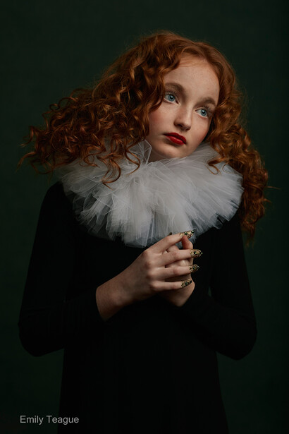 Woman with curly red hair wearing a black garment and white feathered collar against a dark teal background.