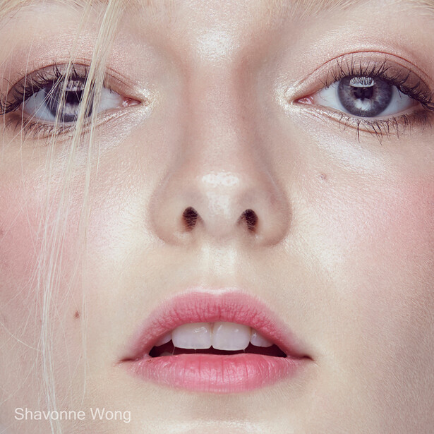 Close-up portrait of a woman's face with pale complexion, pink lips, and blue eyes looking directly at camera.