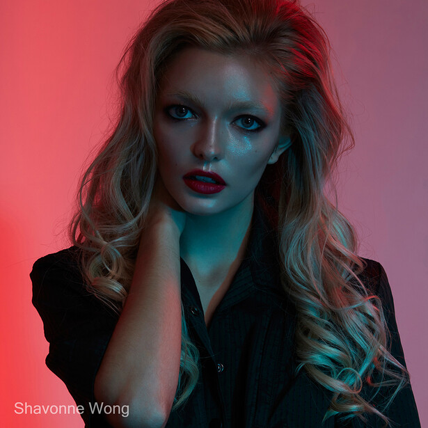 Woman with wavy blonde hair wearing black shirt against red and teal gradient background.