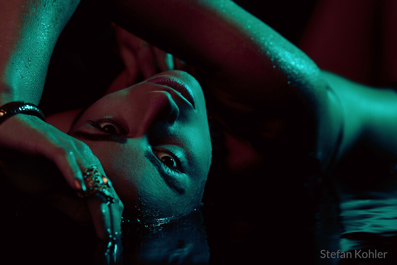 Close-up portrait with cyan and magenta gel lighting creating dramatic shadows across a person's face and shoulders.