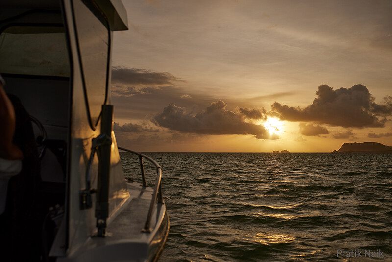 Sunset view from a boat showing golden light breaking through clouds over calm ocean water.