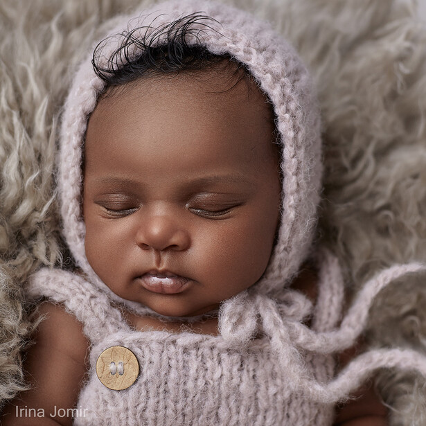 Newborn infant wearing a knitted bonnet and matching sweater with a wooden button detail.