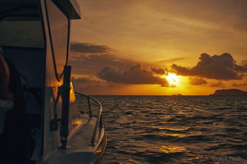 View from a boat's deck toward a dramatic golden sunset over calm ocean waters.