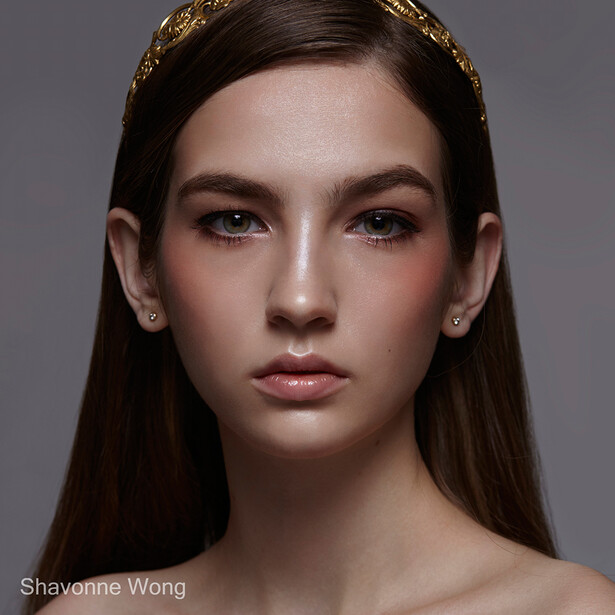 Portrait of a woman with long dark hair and gold headpiece against neutral gray background.