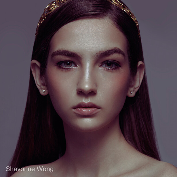 Portrait of a woman with long dark hair against a neutral gray background, lit with soft, even studio lighting.