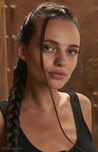 Woman with braided hair wearing black tank top against warm brown backdrop.